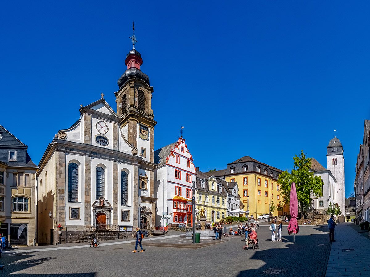 Panoramablick auf den sonnigen Marktplatz in Limburg an der Lahn mit der Stadtkirche St. Sebastian, bunten Fachwerkhäusern und Menschen.