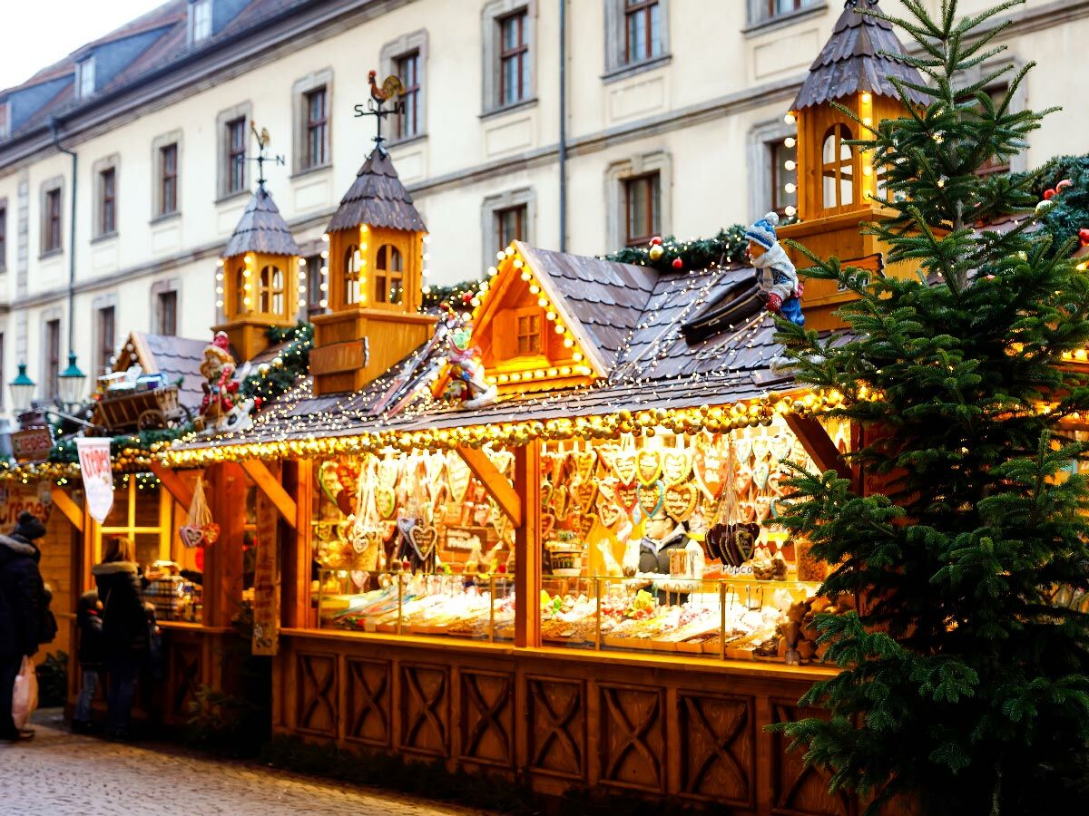Festlich geschmückte Weihnachtsmarktstände mit Lichterketten, Lebkuchenherzen und Weihnachtsbäumen in einer deutschen Stadt.