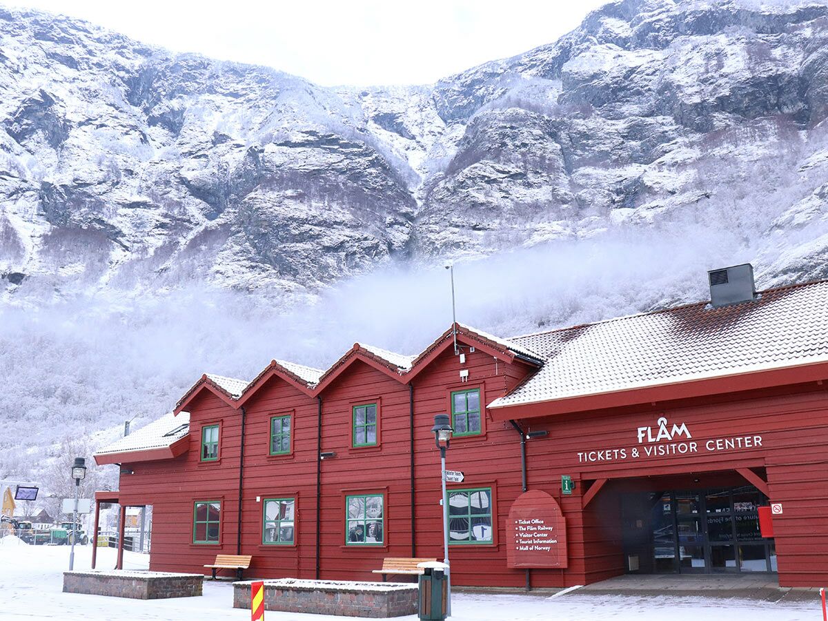Rotes Flåm Tickets &amp; Besucherzentrum im Winter, umgeben von schneebedeckten Bergen und Nebel in Norwegen.