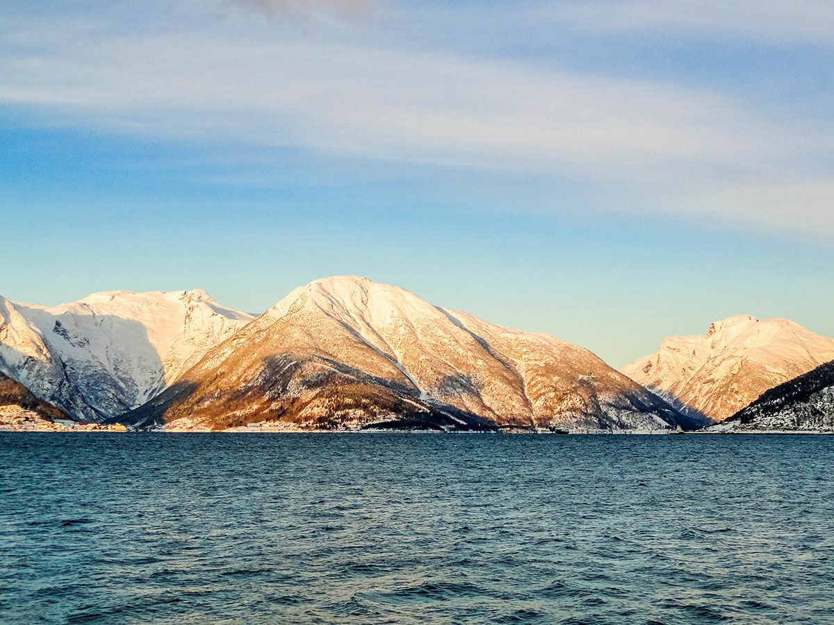 Panorama von schneebedeckten Bergen, die sich in einem ruhigen Fjord spiegeln, unter einem klaren blauen Winterhimmel.