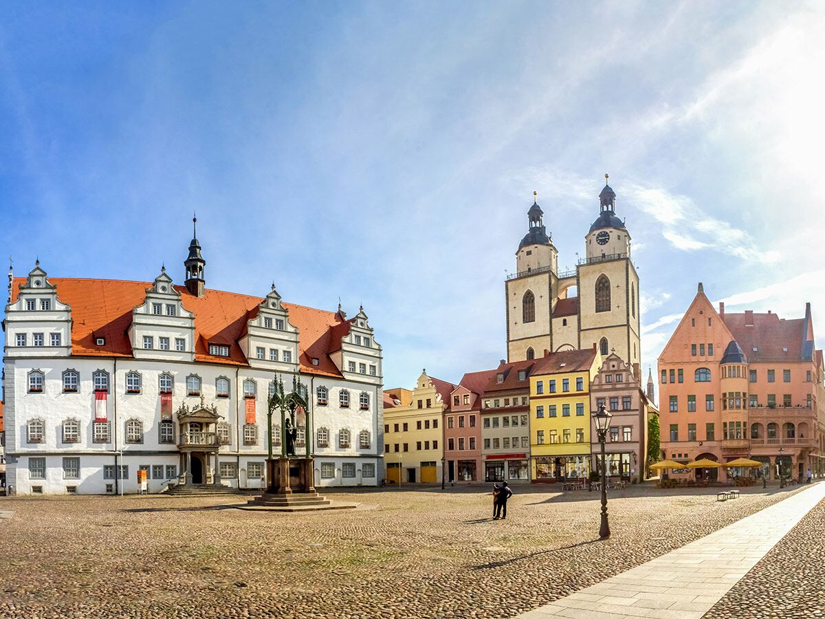 Historischer Marktplatz in Wittenberg mit Altem Rathaus, Marienkirche und bunten Gebäuden unter blauem Himmel.
