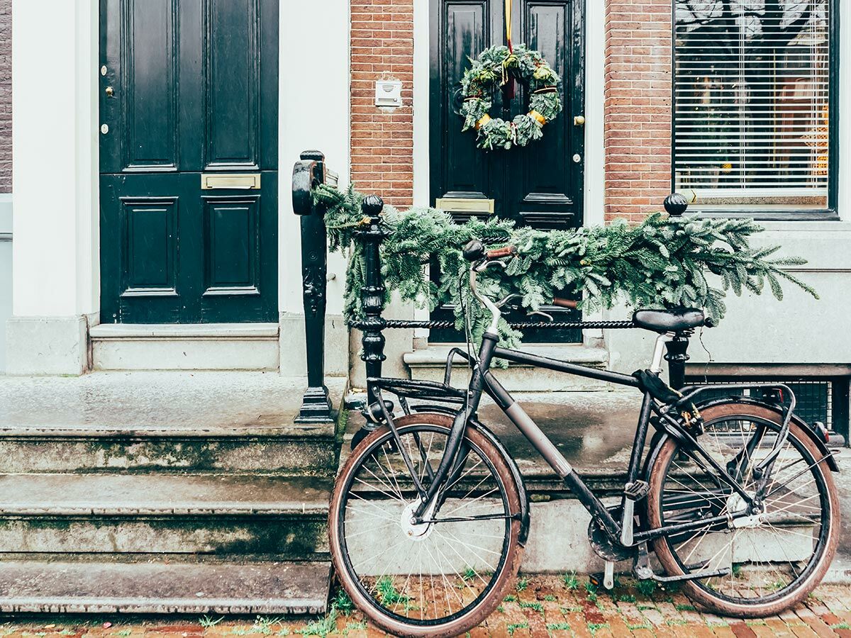 Fahrrad mit Tannengirlande vor zwei verzierten Haustüren in Amsterdam mit Weihnachtskranz und Stufen.