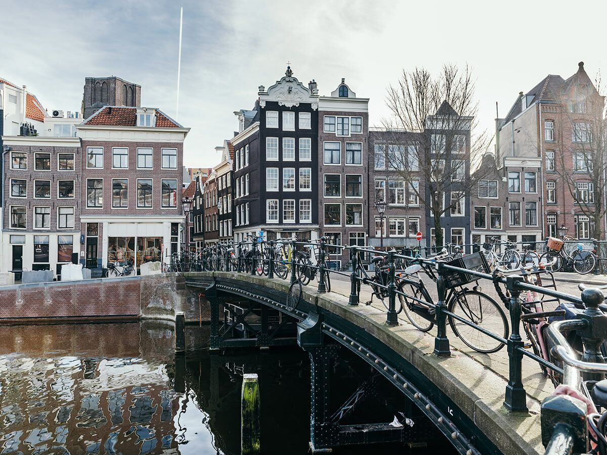 Historische Kanalbrücke in Amsterdam mit vielen geparkten Fahrrädern und traditionellen Grachtenhäusern unter hellem Himmel.