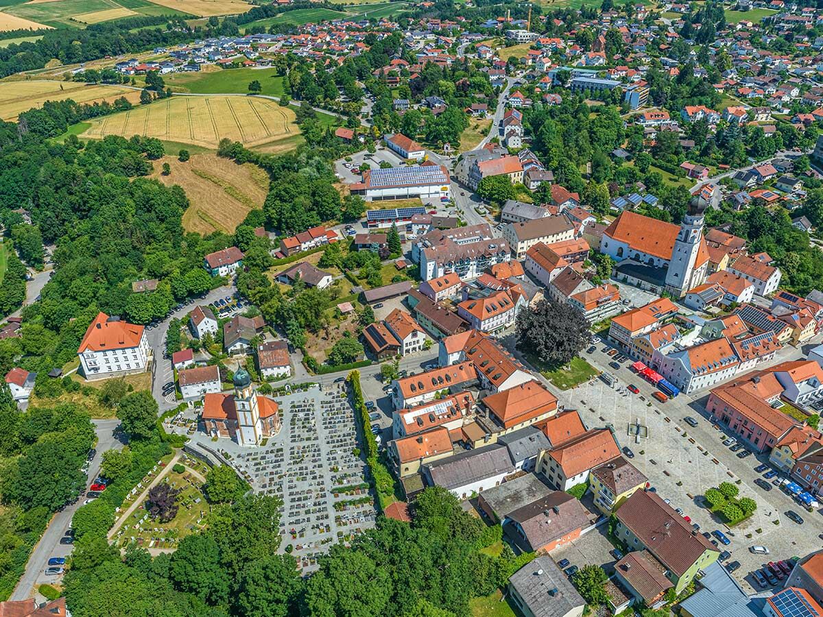 Luftaufnahme einer malerischen europäischen Kleinstadt mit Kirche, Marktplatz, Wäldern und Feldern unter blauem Himmel.