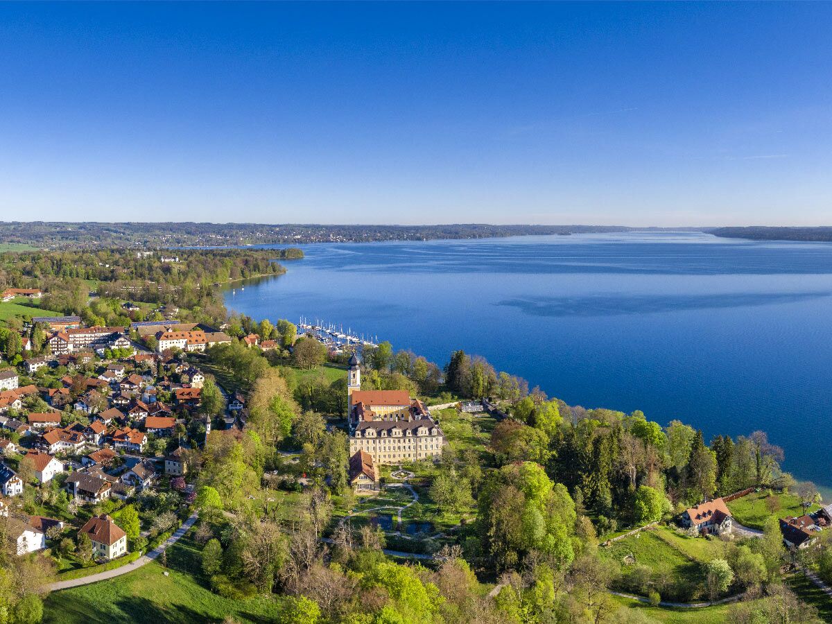 Luftaufnahme von Schloss Berg am Starnberger See, umgeben von einem Dorf, grünen Wäldern und einem Yachthafen.