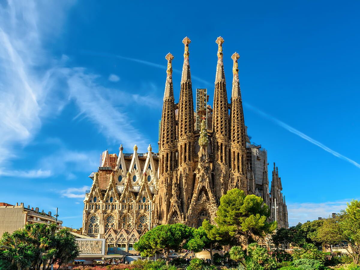 Majestätische Sagrada Familia in Barcelona mit blauen Himmel und grünen Bäumen unter der Sonne.