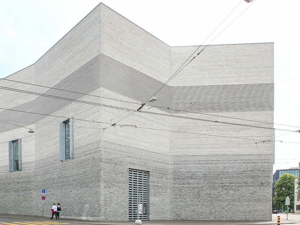 Modernes Gebäude mit auffälliger gestreifter Fassade und Fenstern in einer Stadtlandschaft mit Stromleitungen und Fußgängern.