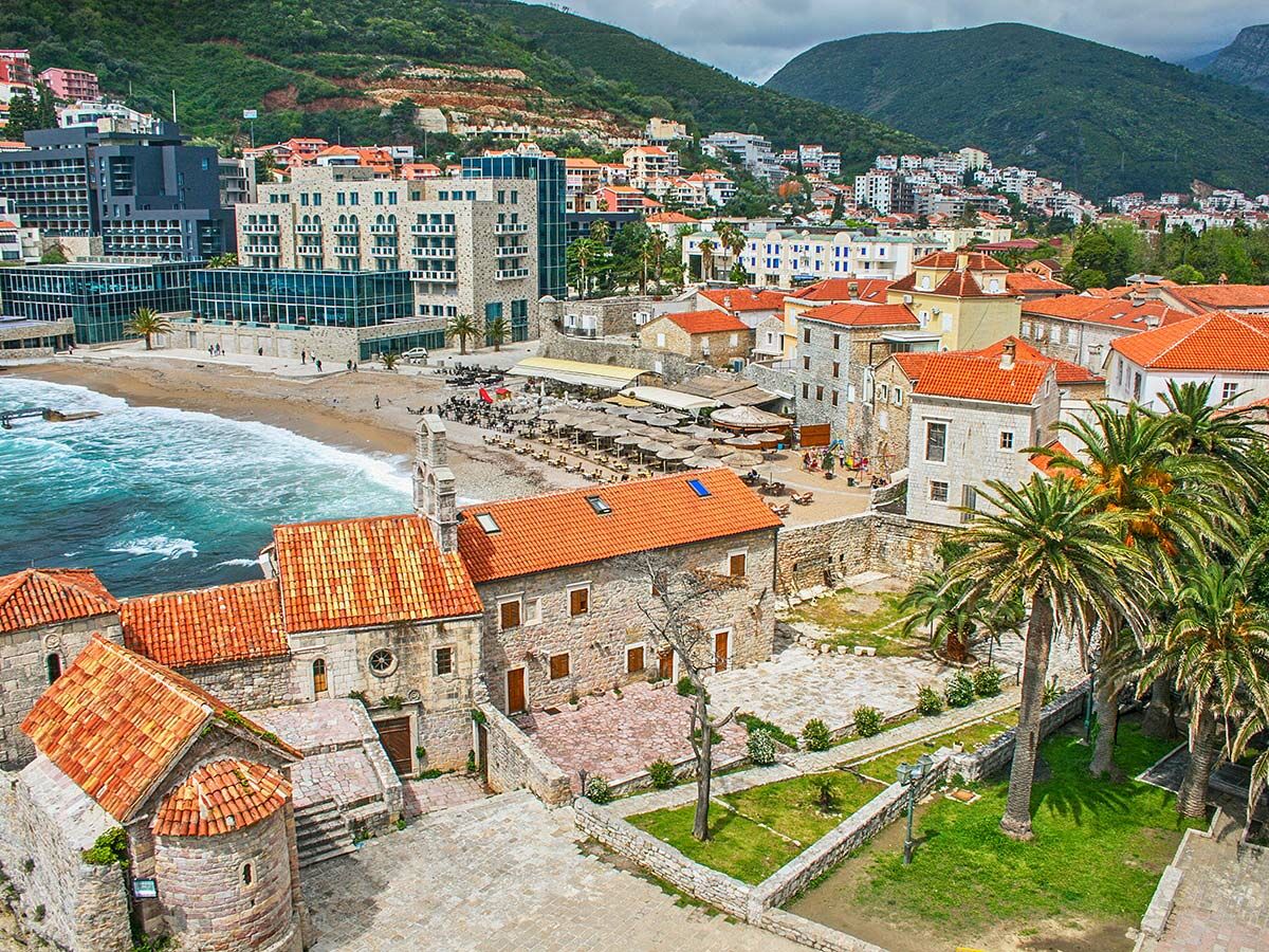 Luftbild von Budva, Montenegro, mit historischer Altstadt, Strand, türkisfarbenem Meer und grünen Bergen im Hintergrund.