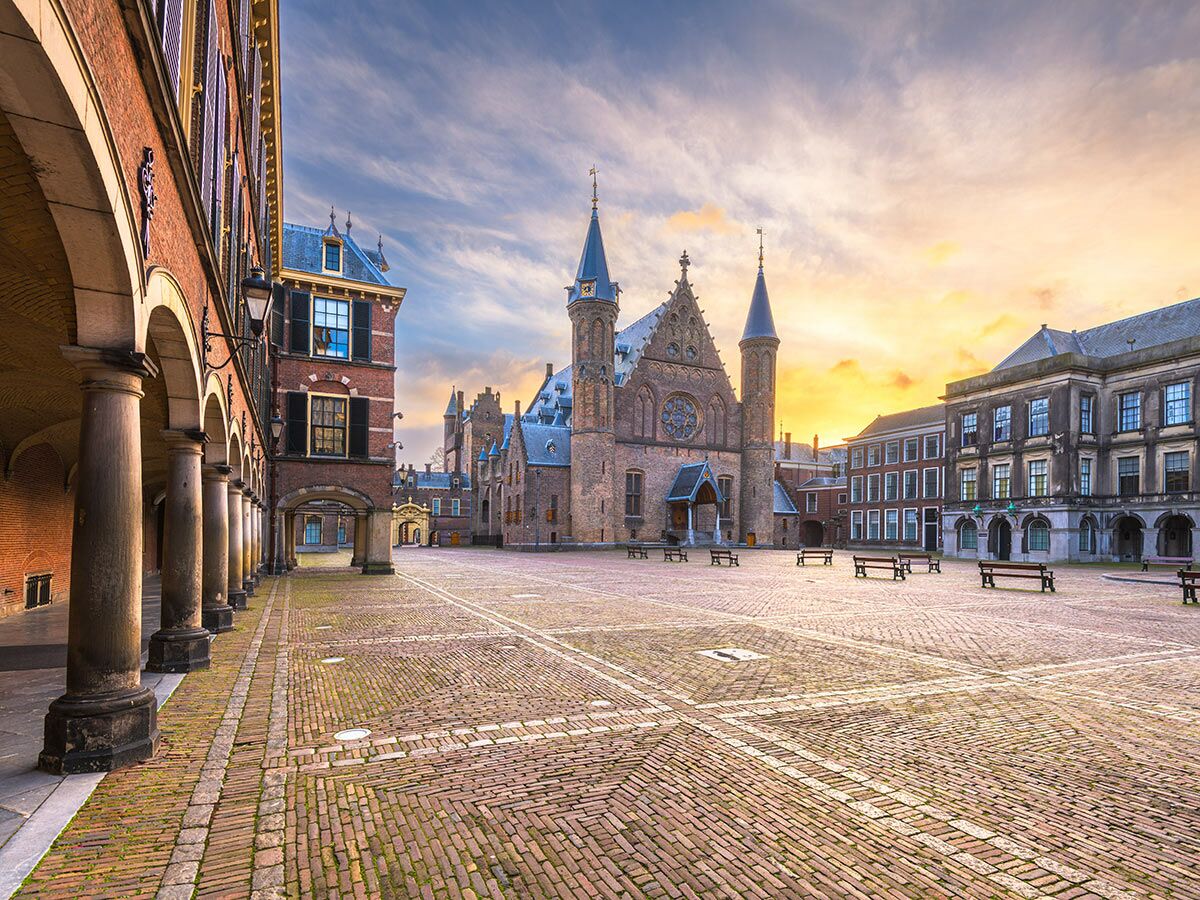 Historischer Binnenhof in Den Haag bei Sonnenuntergang mit Ridderzaal, Regierungsgebäuden und Säulengang im goldenen Licht.