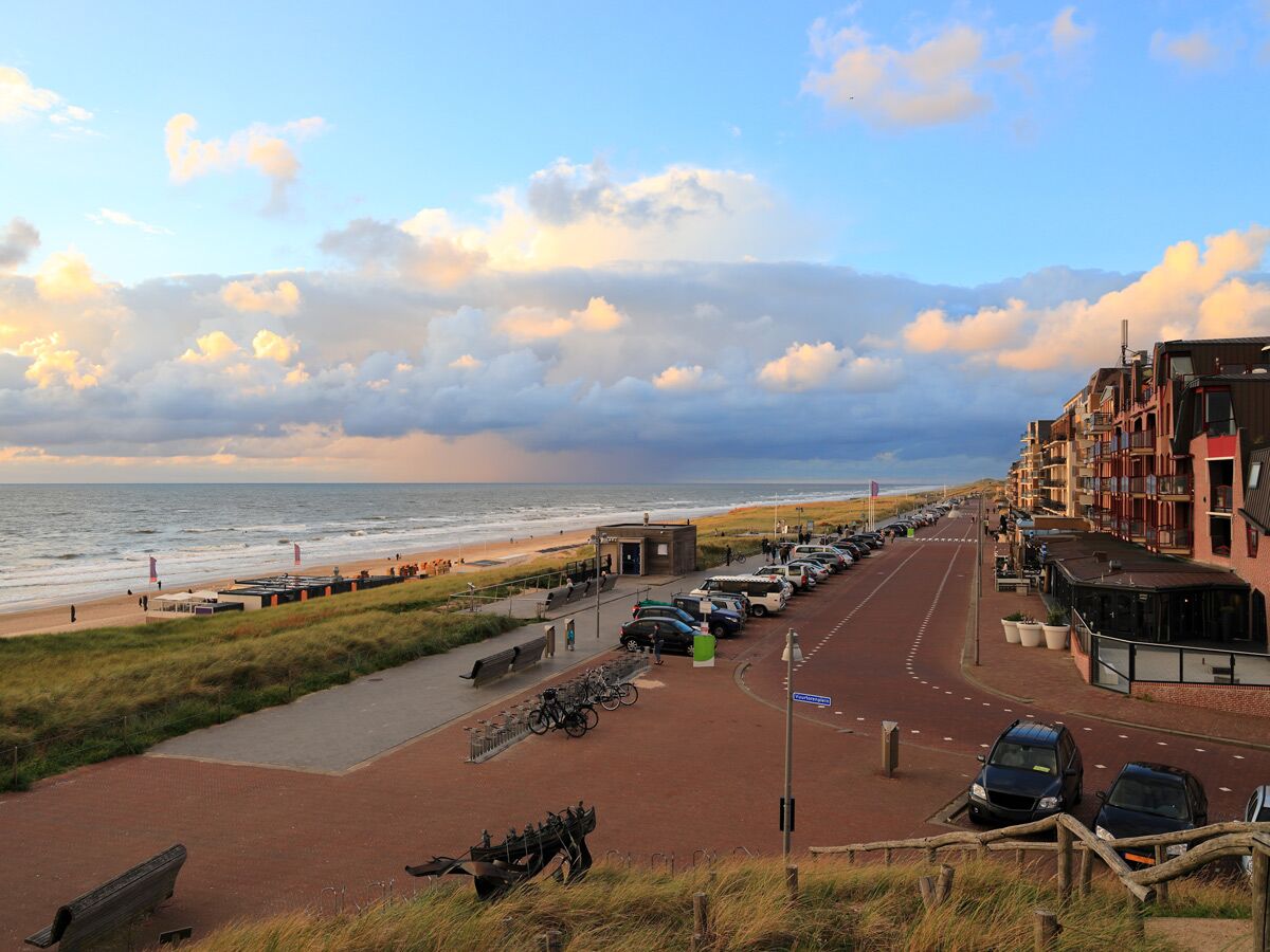 Blick auf den Strand, die Dünen und die Promenade von Renesse, Niederlande, mit geparkten Autos und Gebäuden am Abend.