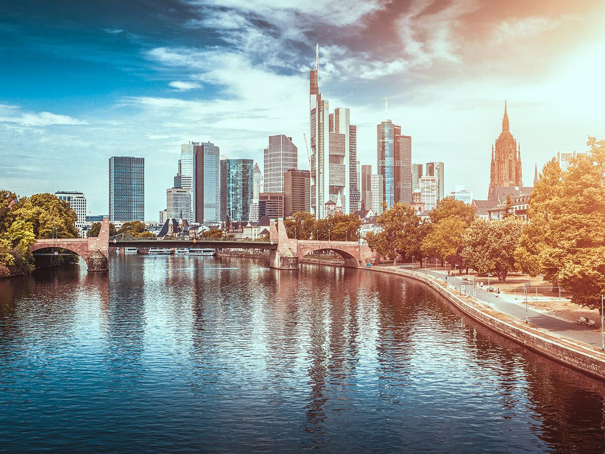 Panoramablick auf die Frankfurter Skyline mit modernen Hochhäusern, dem Main, Brücken und dem Dom unter blauem Himmel.