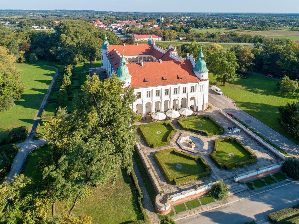 Luftbild eines weißen Schlosses mit rotem Dach und grünen Türmen, umgeben von einem formalen Garten, Park und Landschaft.
