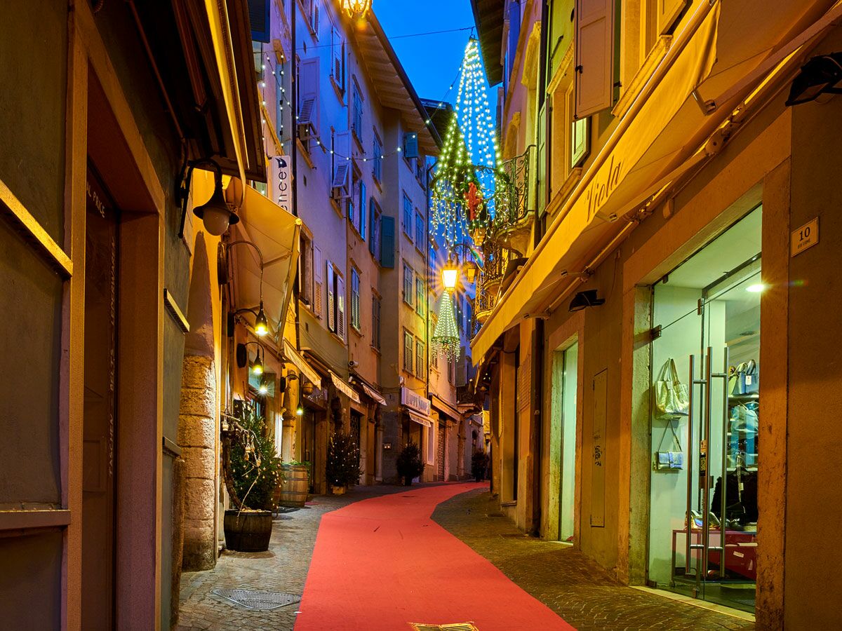 Festlich beleuchtete Gasse bei Nacht mit rotem Teppich, Geschäften, Weihnachtsdekorationen und leuchtenden Tannenbäumen.