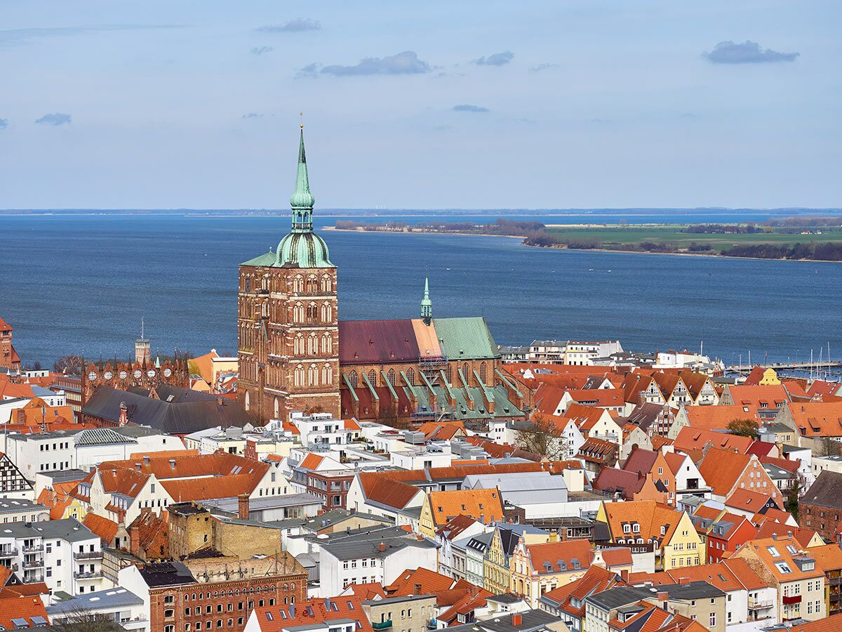 Panoramablick auf die historische Altstadt von Stralsund mit der Marienkirche, roten Dächern und dem Strelasund im Hintergrund.