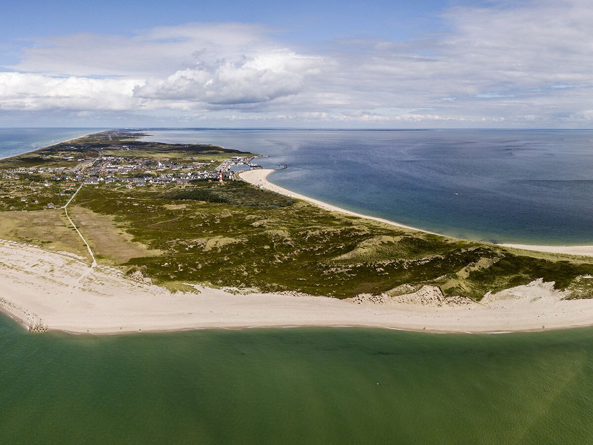 Luftbild von List auf Sylt zeigt Hafen, Stadt, Sandstrände, grünes Wattenmeer und blaue Nordsee unter bewölktem Himmel.
