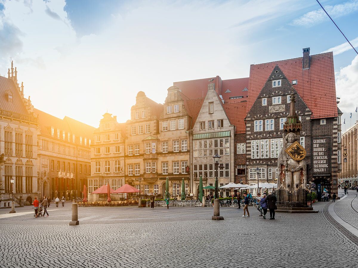 Historischer Marktplatz Bremen mit Rolandstatue, historischen Gebäuden und Menschen im warmen Abendlicht.