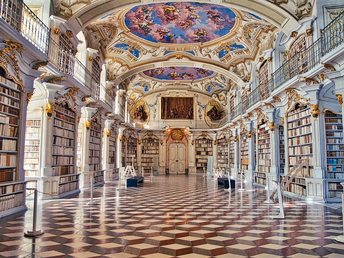 Barocke Klosterbibliothek Admont mit hohen Bücherregalen, Deckenfresken, goldenen Verzierungen und gemustertem Boden.