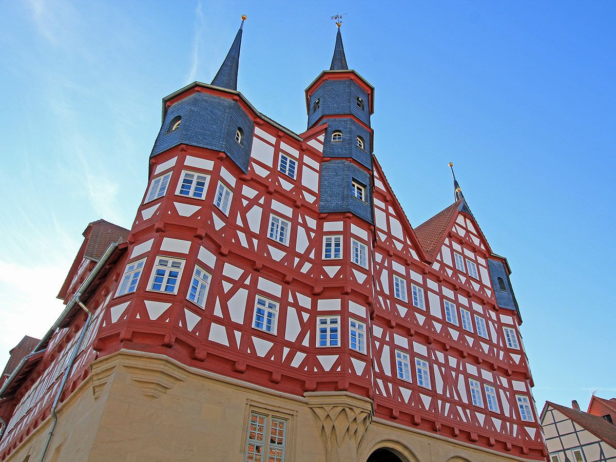Detailreiches rot-weißes Fachwerkhaus mit zwei spitzen Türmen, blauen Schieferdächern und vielen Fenstern unter klarem Himmel.