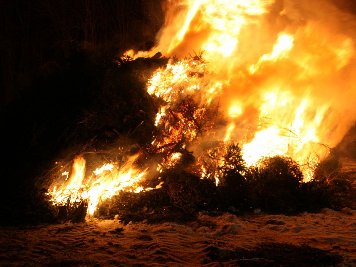 Großes Osterfeuer brennt nachts, hohe Flammen lodern über Ästen und Reisig auf schneebedecktem Boden.