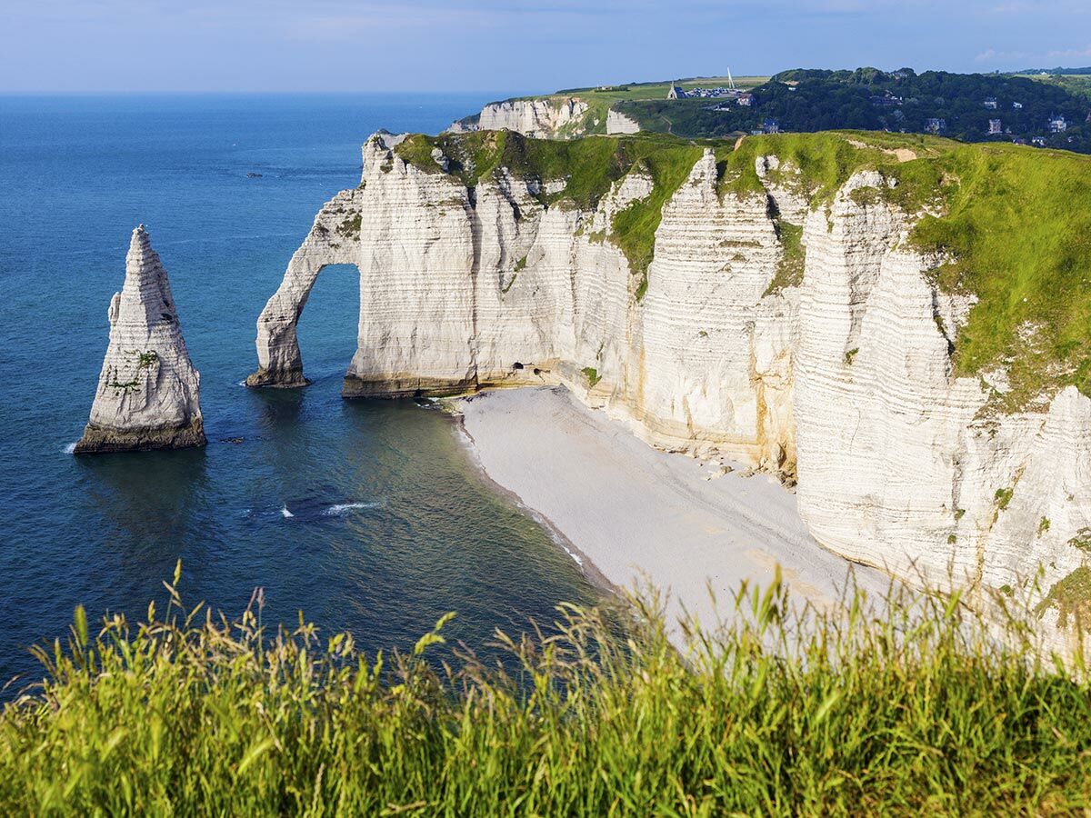 Dramatische weiße Kreidefelsen und ein natürlicher Felsbogen in Étretat, Frankreich, mit blauem Meer und Strand.