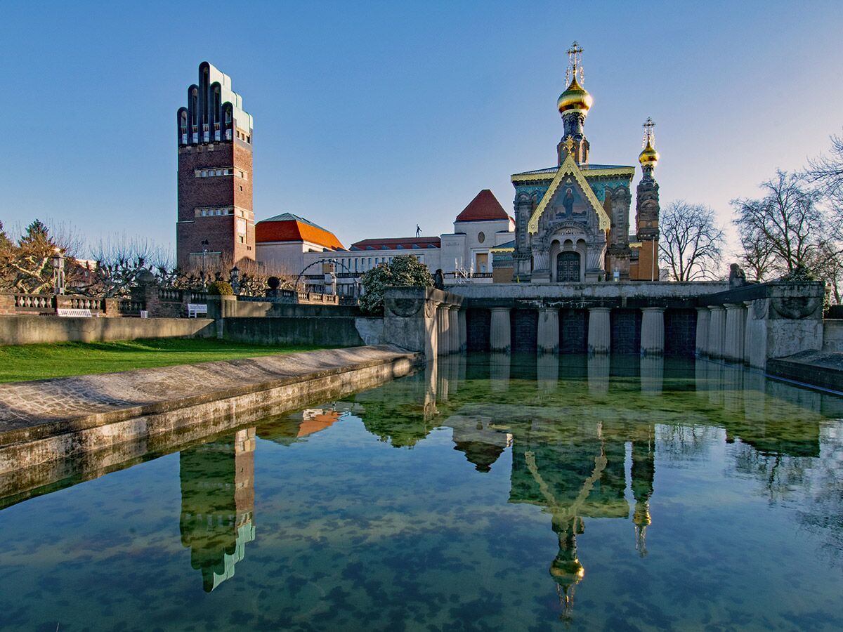 Mathildenhöhe Darmstadt: Hochzeitsturm und Russische Kapelle spiegeln sich im Wasserbecken unter blauem Himmel.