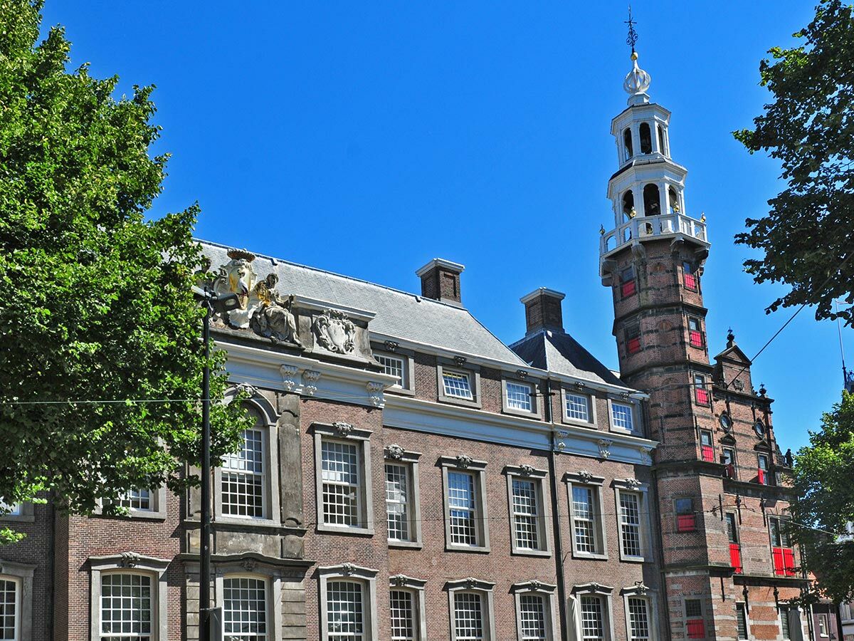 Historisches Backsteingebäude mit elegantem weißen Turm und Spire unter klarem blauem Himmel, umrahmt von grünen Bäumen.