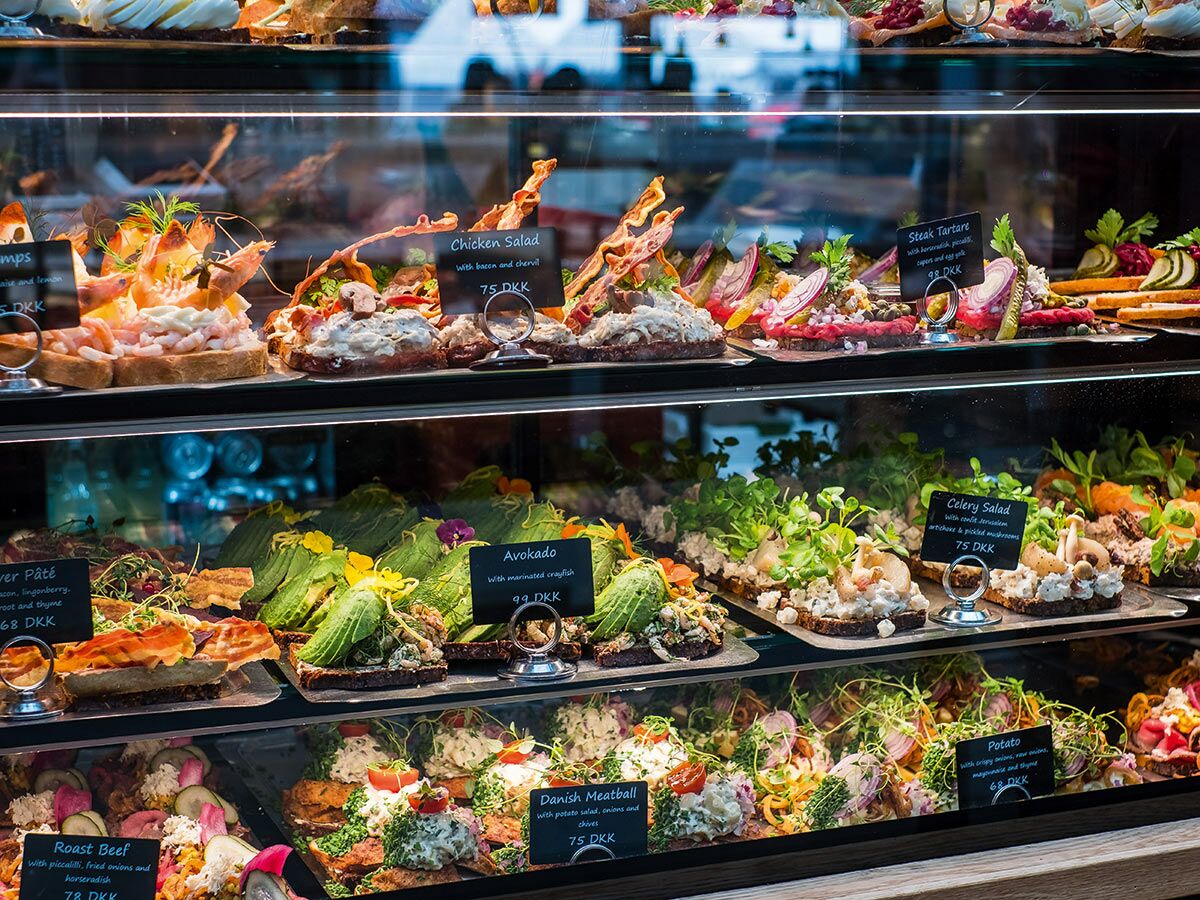 Nahaufnahme einer reichhaltigen Auslage mit verschiedenen dänischen Smørrebrød, darunter Shrimps, Steak Tartare und Avocado.