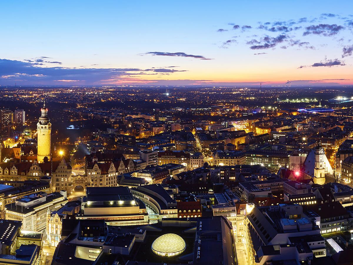 Panoramablick auf Leipzig bei Dämmerung mit dem beleuchteten Neuen Rathaus, der Altstadt und dem urbanen Lichtermeer.