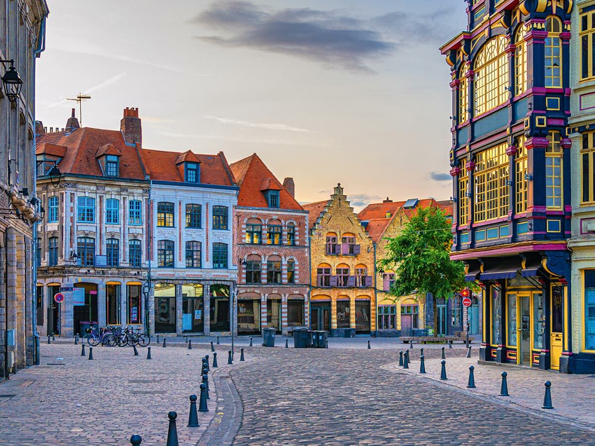 Historischer Stadtplatz in Lille mit bunten Giebelhäusern und Kopfsteinpflaster in der Abenddämmerung. Fahrräder stehen am Rand.