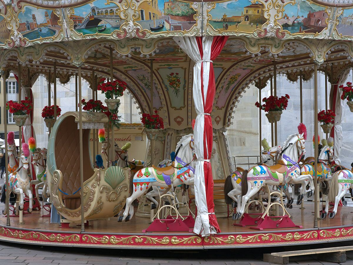 Detailansicht eines nostalgischen Karussells mit bemalten Pferden, einer eleganten Kutsche und floralen Verzierungen.