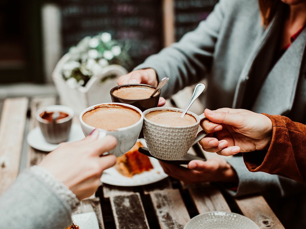 Drei Freunde stoßen im Café an einem Holztisch mit warmen Kaffeegetränken an. Eine gemütliche Kaffeepause im Freien.