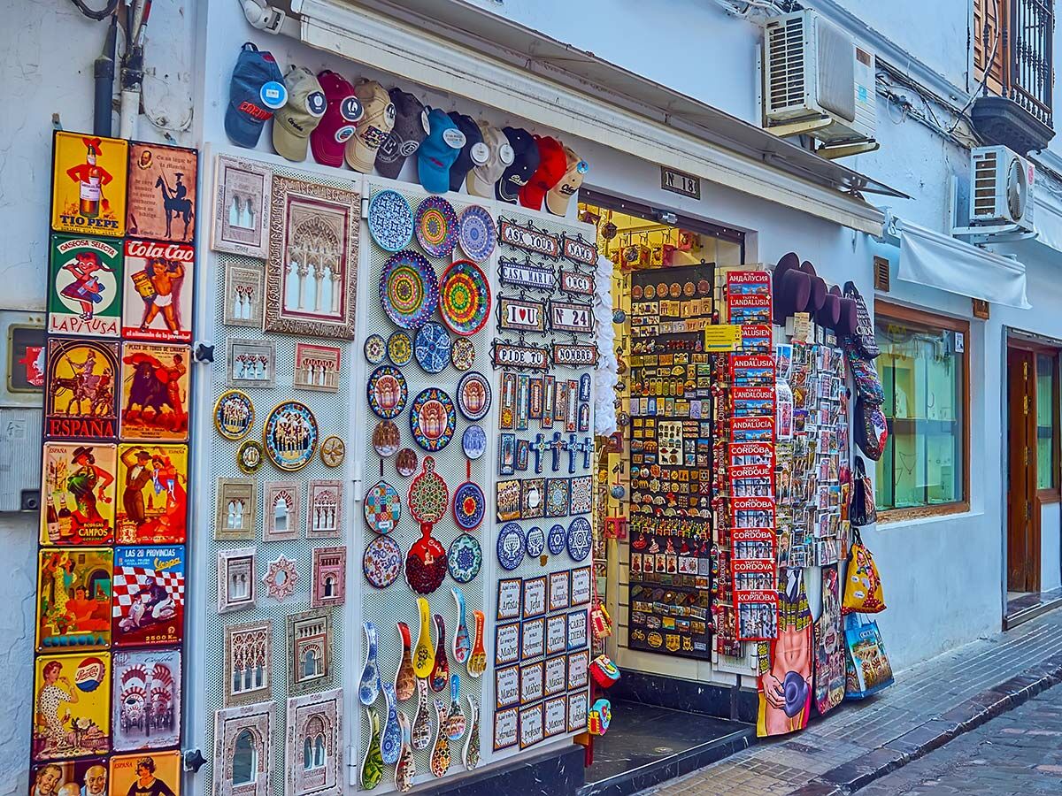 Bunter spanischer Souvenirladen mit Hüten, Keramik, Vintage-Schildern und vielen traditionellen Artikeln an einer weißen Wand.