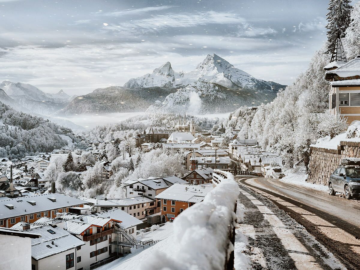 Panoramaansicht einer verschneiten Bergstadt in den bayerischen Alpen mit Watzmann, Häusern, Kirche und Straße im Winter.