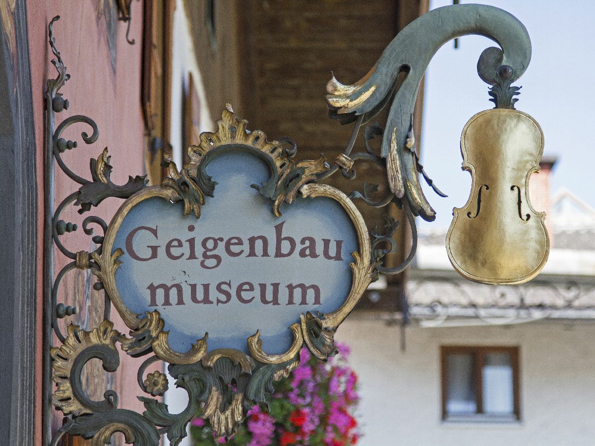 Ornates Geigenbau Museum Schild mit goldener Geige und barocken Verzierungen vor einem historischen Gebäude.