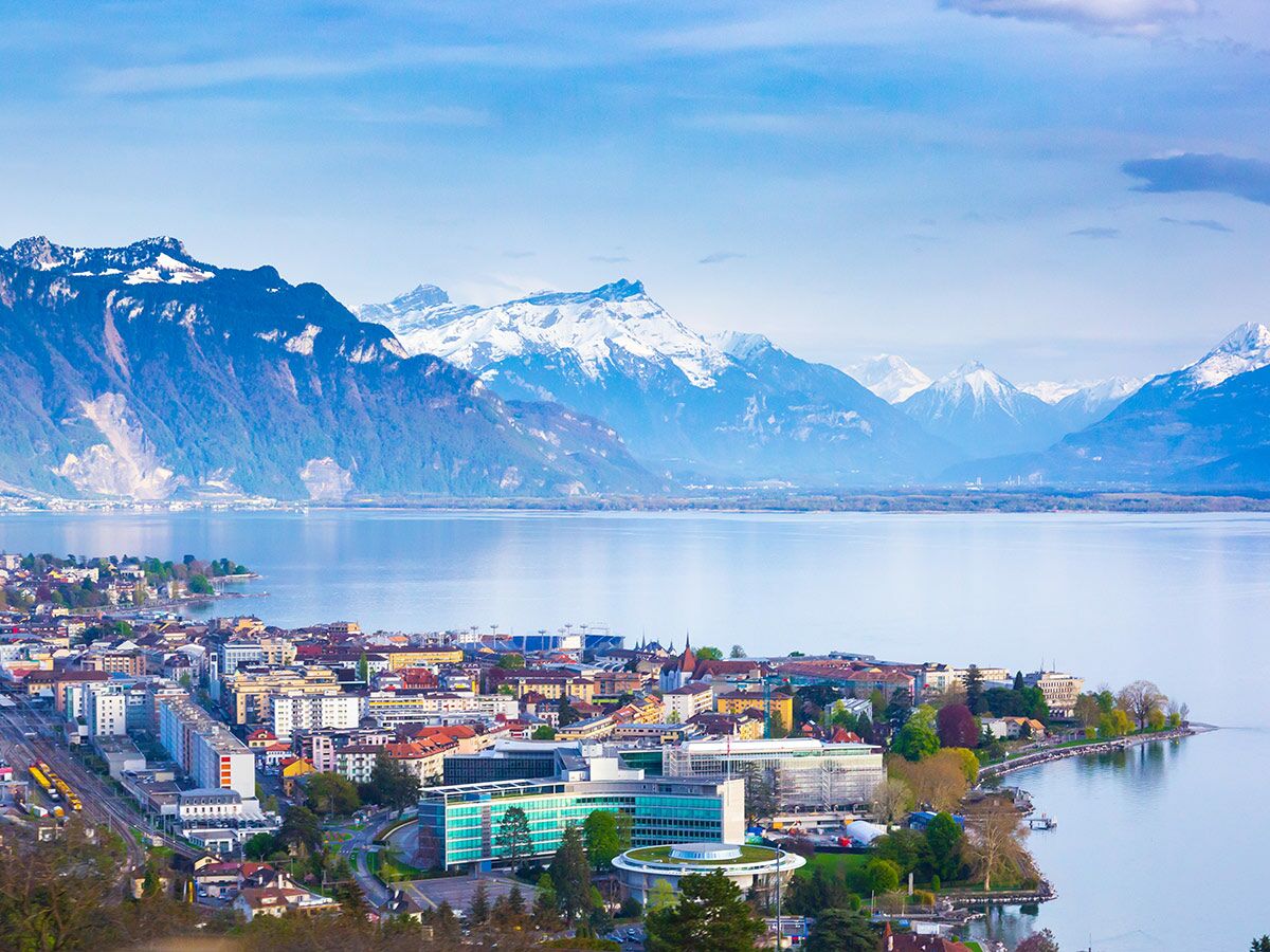 Panoramablick auf Vevey am Genfersee mit Gebäuden, Bahnhof und Nestlé-Hauptsitz, umgeben von den Schweizer Alpen.