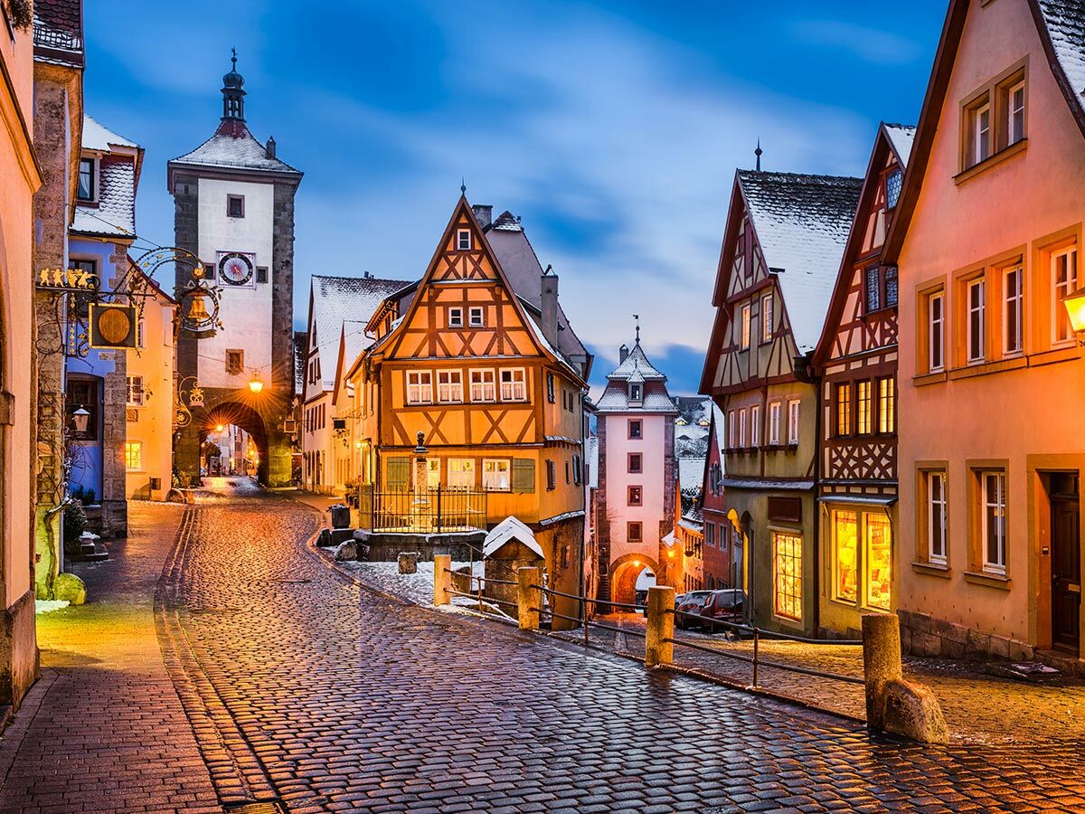 Winterliche Altstadtgasse in Rothenburg ob der Tauber bei Dämmerung mit Fachwerkhäusern, Kopfsteinpflaster und beleuchtetem Turm.