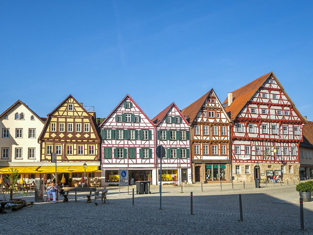 Reihe bunter Fachwerkhäuser am sonnigen Marktplatz in einer deutschen Altstadt mit Menschen in Cafés.