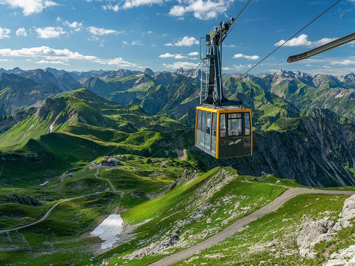 Gelbe Nebelhorn Seilbahn schwebt über grüne Allgäuer Alpen mit weiten Tälern, Wanderwegen und blauem Himmel.
