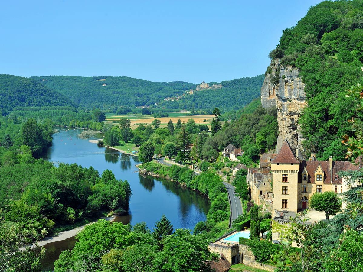 Panoramablick auf die Dordogne mit malerischem Dorf, historischen Felsgebäuden, Schloss und grünen Hügeln in Frankreich.