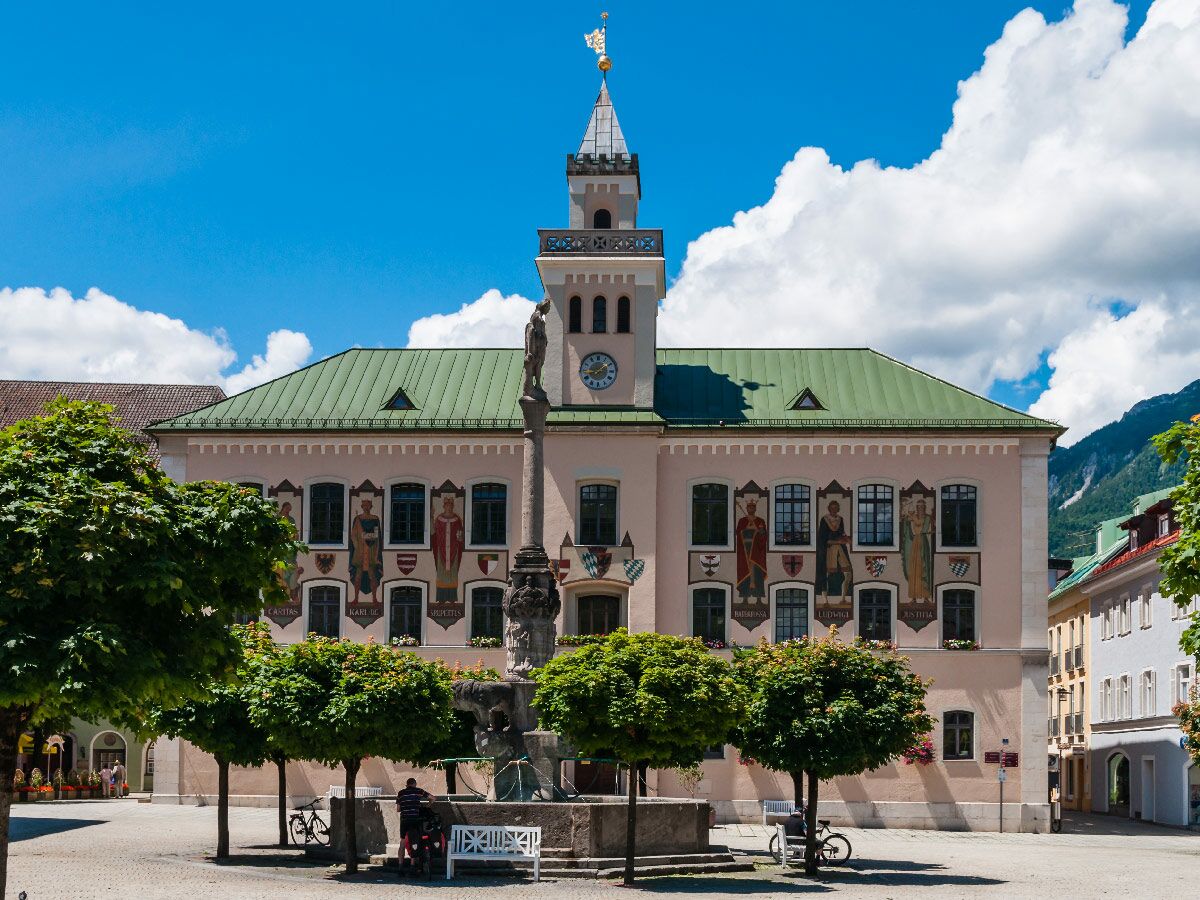 Historisches Rathaus Garmisch-Partenkirchen am sonnigen Marktplatz mit Brunnen, bemalter Fassade, Turm und Menschen.