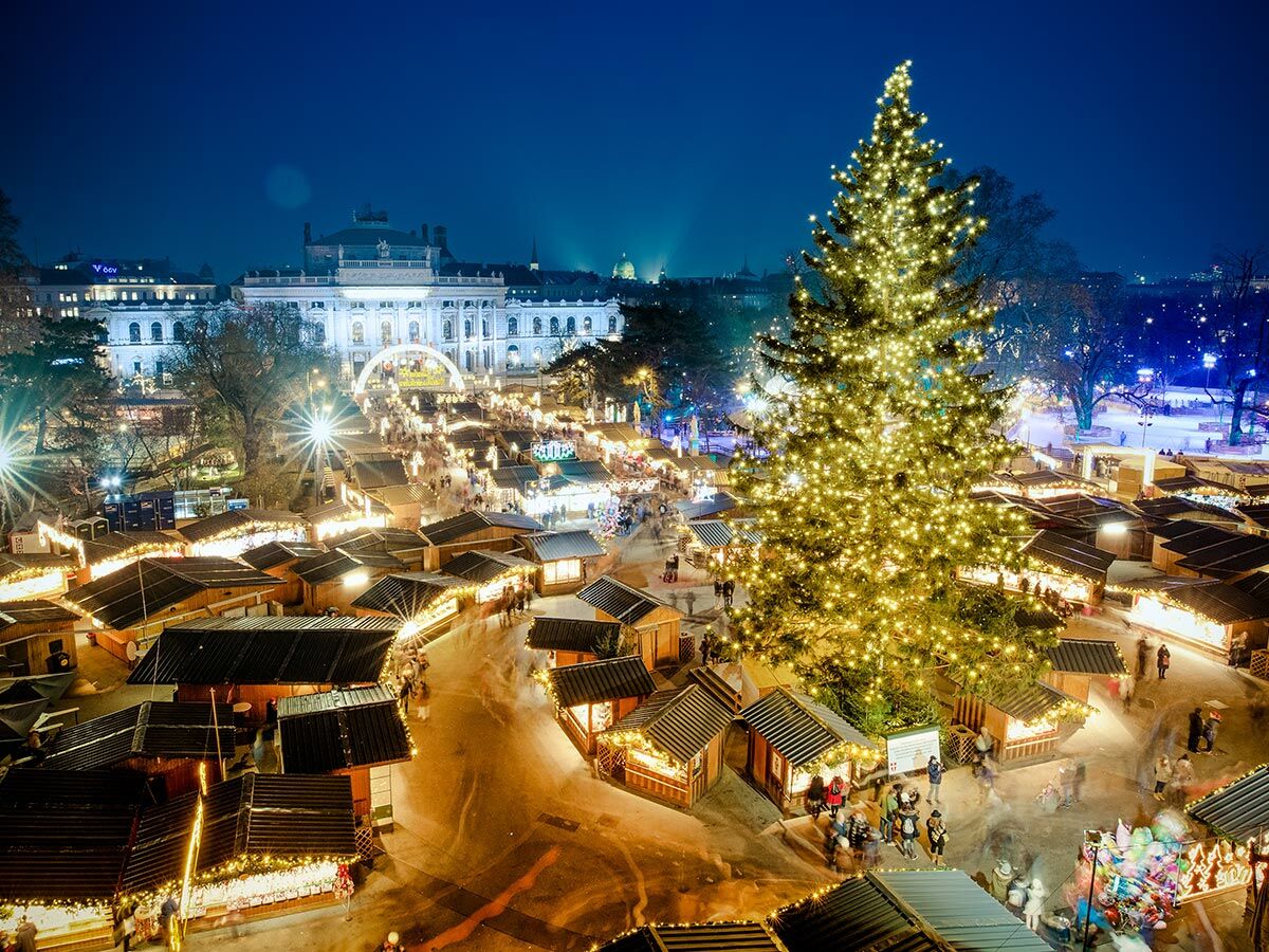 Festlicher Weihnachtsmarkt in Wien vor dem Rathaus bei Nacht, mit leuchtendem Christbaum und geschäftigen Buden.
