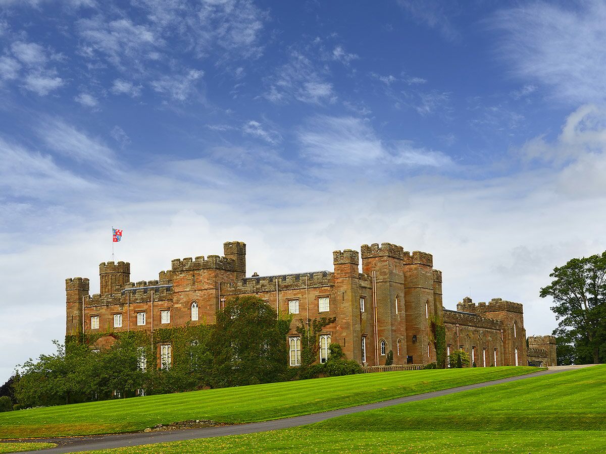 Scone Palace in Schottland, ein historisches Schloss mit roten Sandsteintürmen, umgeben von grünen Rasenflächen unter blauem Himmel.
