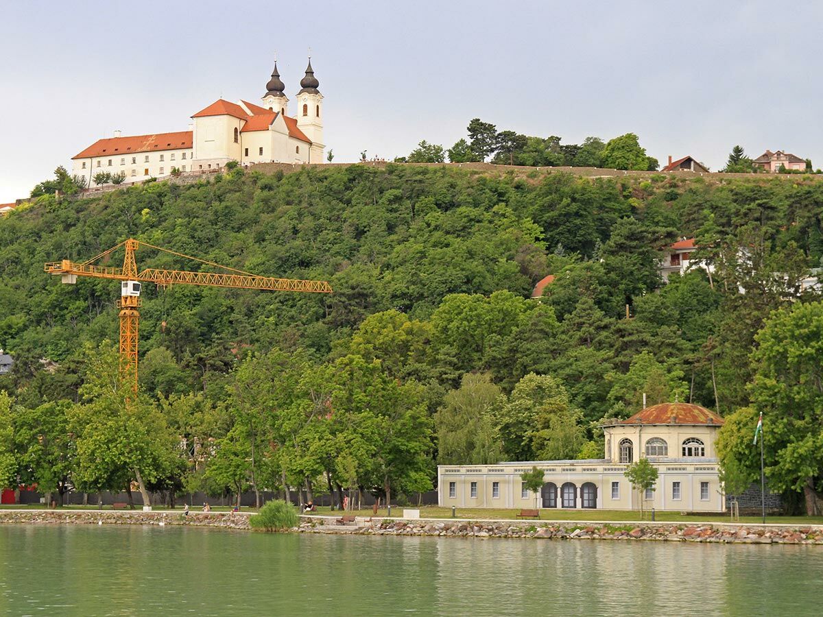 Benediktinerabtei Tihany auf grünem Hügel über dem Plattensee. Gelber Baukran und Gebäude am Ufer.