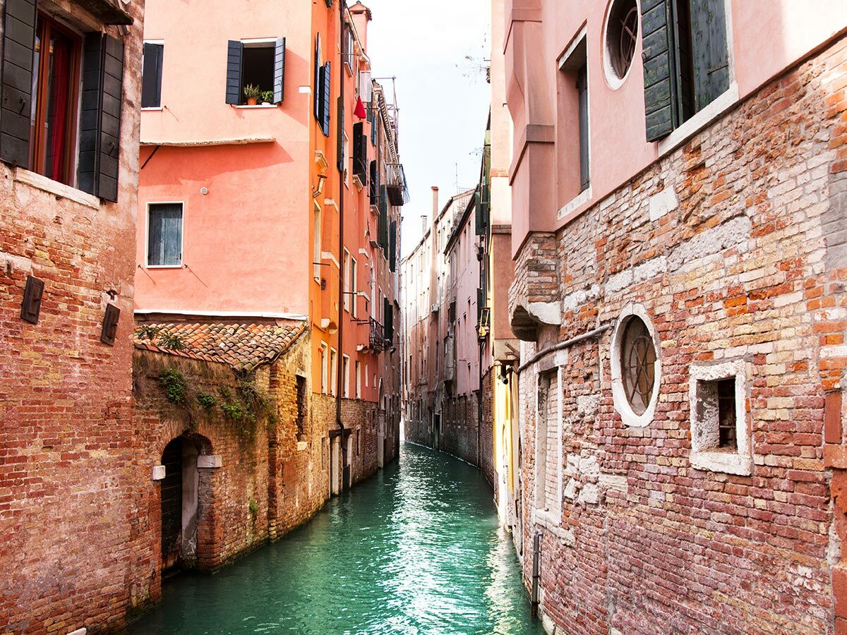 Venedig: Alter, schmaler Kanal umgeben von historischen Backsteingebäuden mit Fensterläden und klarem, türkisem Wasser.