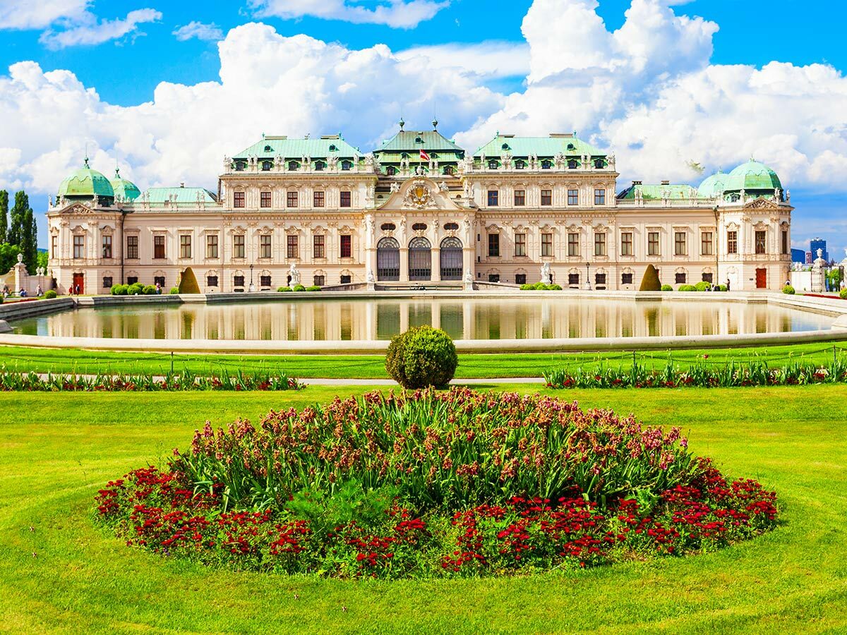 Oberes Belvedere Schloss in Wien mit großem Teich, grünen Gärten, Blumen und blauem Himmel.