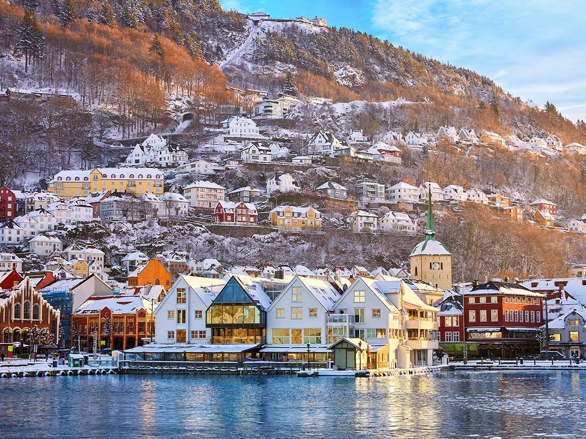Bergen Norwegen im Winter: Eine malerische Stadtansicht mit schneebedeckten Häusern, Hafen, Bergen und einer Kirche bei Sonnenschein.