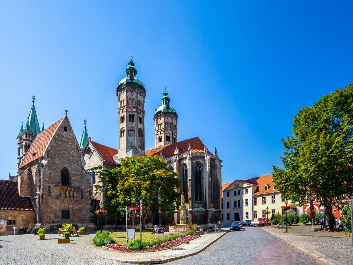 Panoramablick auf den Naumburger Dom und Altstadtplatz an einem sonnigen Tag mit Bäumen und historischen Gebäuden.
