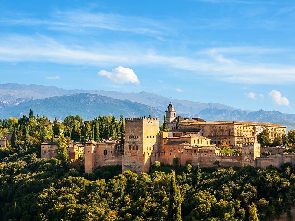 Alhambra in Granada, Spanien, mit historischen Palästen und Festung inmitten grüner Bäume und vor Bergkulisse.
