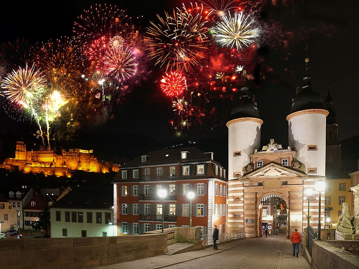 Nächtliches Feuerwerk über Heidelberger Schloss und Brückentor der Alten Brücke mit beleuchteten Gebäuden.