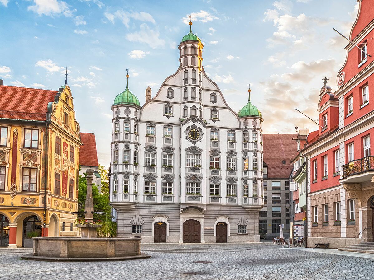 Historisches Rathaus Schongau mit grünen Kuppeln, Uhr und Brunnen auf dem sonnigen Marktplatz.
